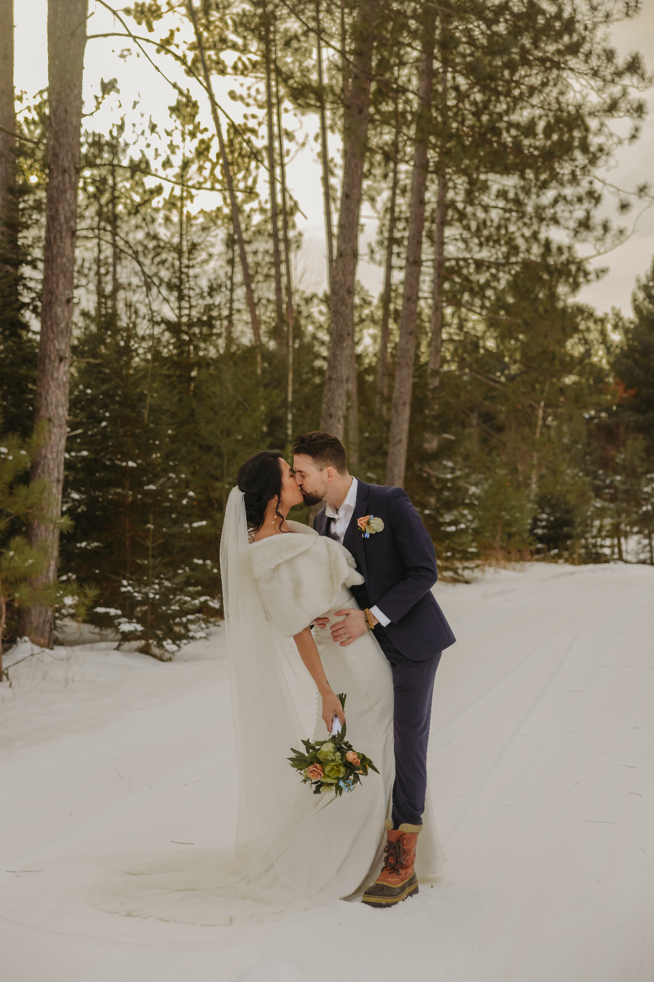 Bride and groom kissing in snowy forest