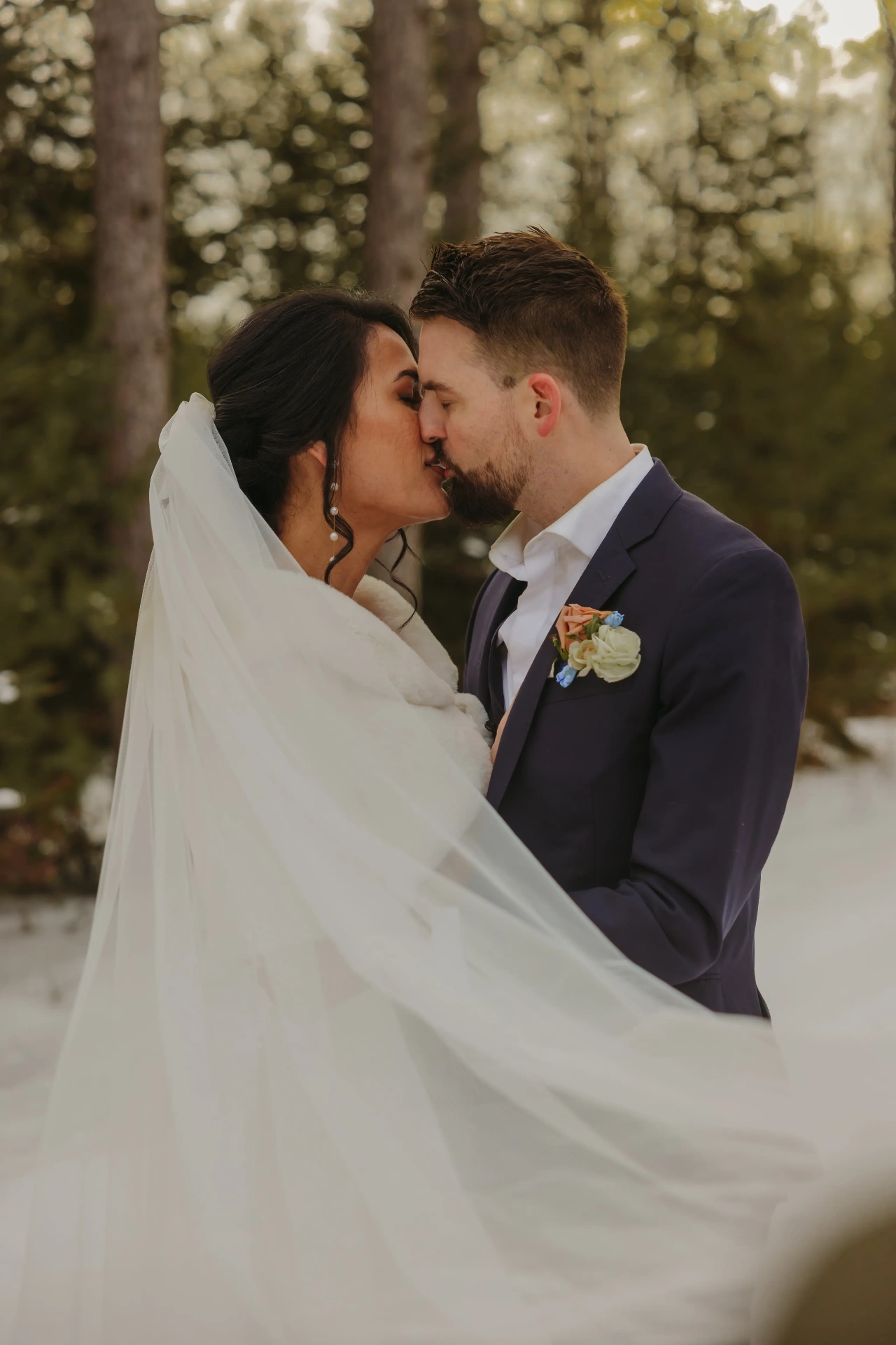 Bride and groom kissing with flowing veil in snowy forest