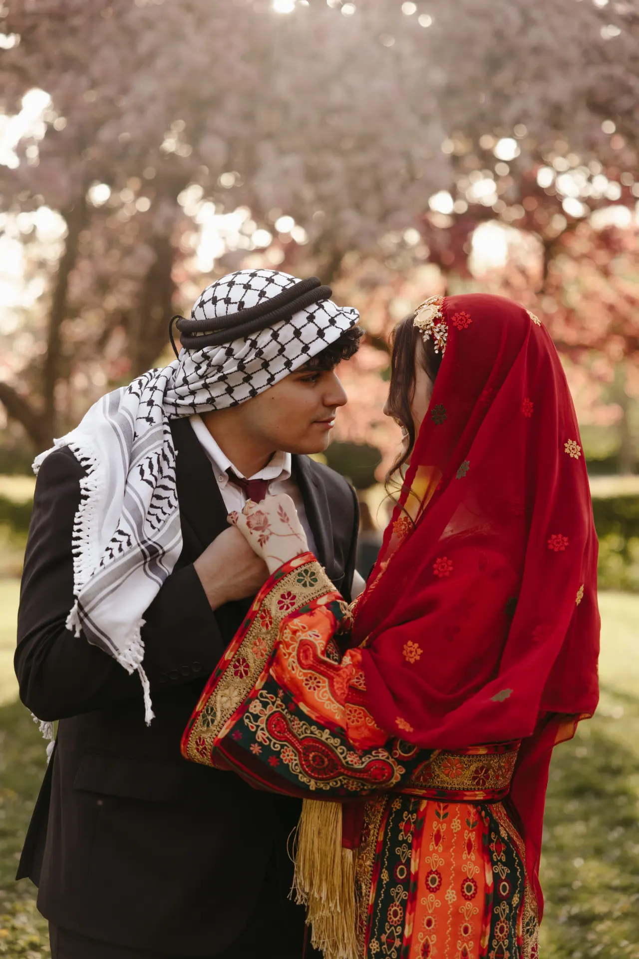 Bride in a red embroidered thobe facing her groom in a keffiyeh beneath blossoming trees — Minneapolis & Twin Cities wedding photography by Emma Ziegler, Honey Deww Photography (Minnesota)