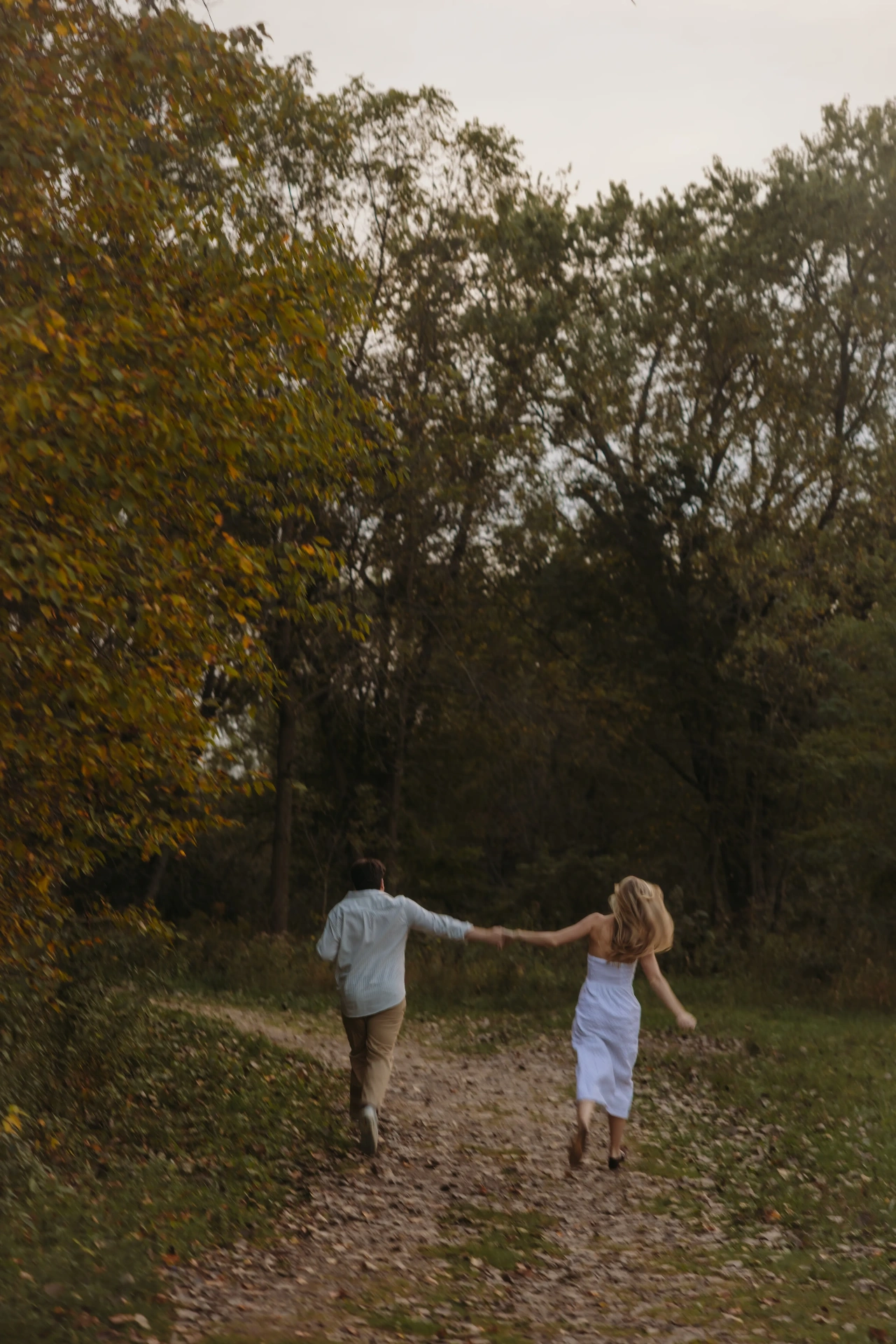Couple running hand in hand down autumn leaf-covered path