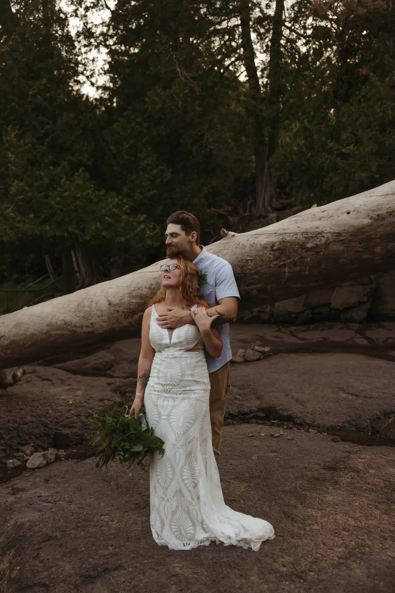 Groom standing behind his bride on the rock ledge above a waterfall, fern bouquet in hand — Minneapolis & Twin Cities wedding photography by Emma Ziegler, Honey Deww Photography (Minnesota)