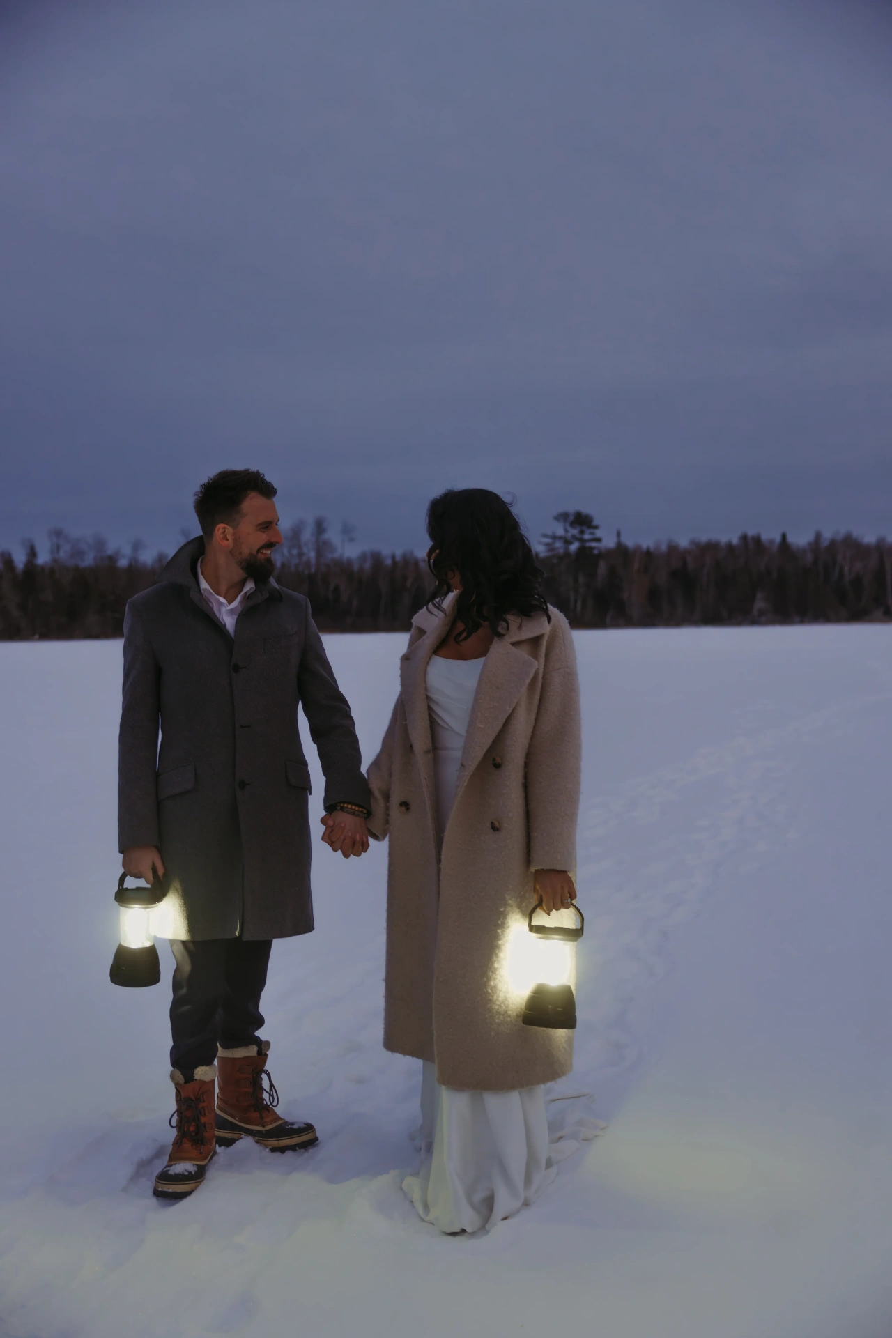 Couple holding lanterns walking in snow at dusk