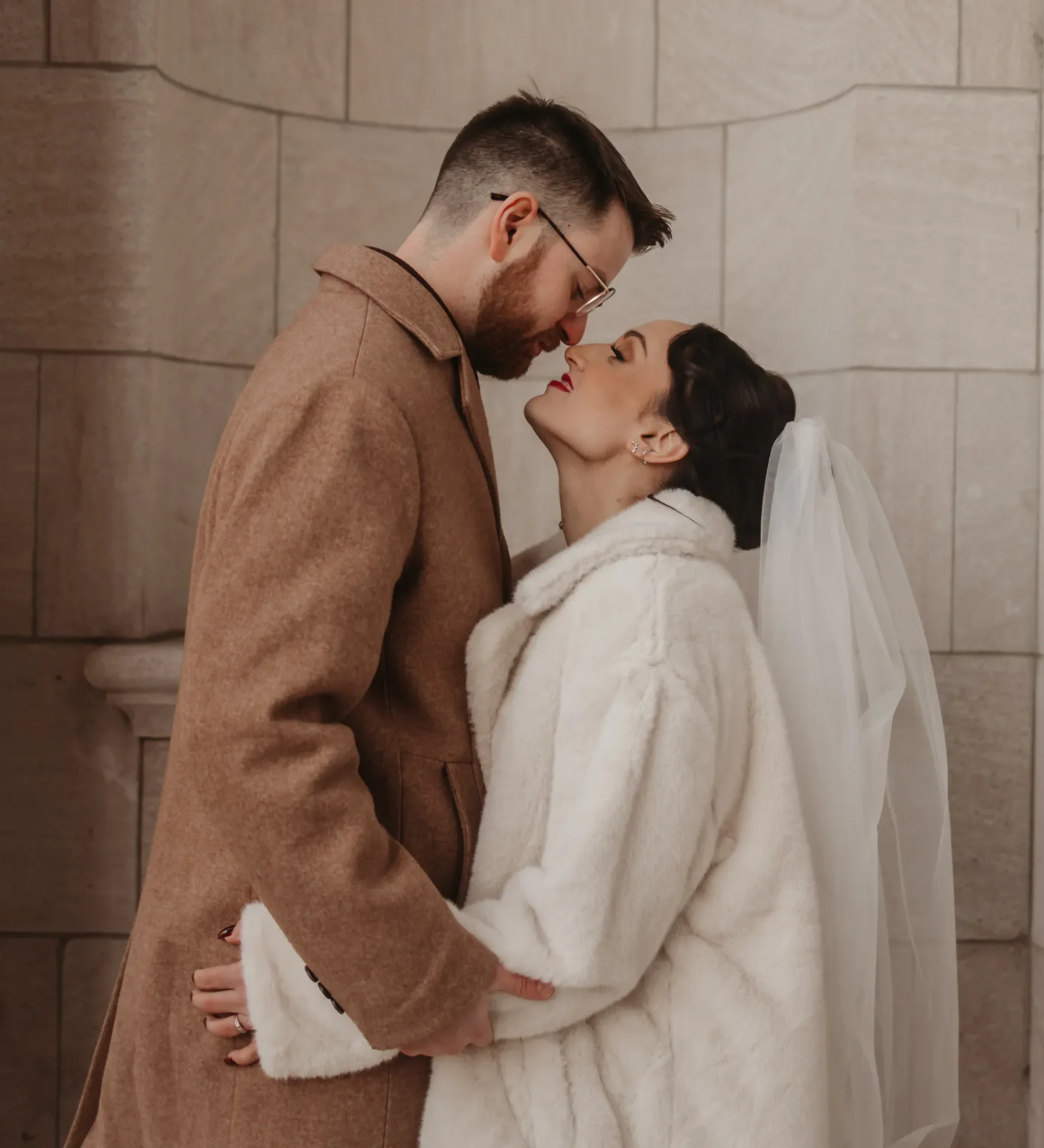 Couple in coats sharing intimate moment by stone wall