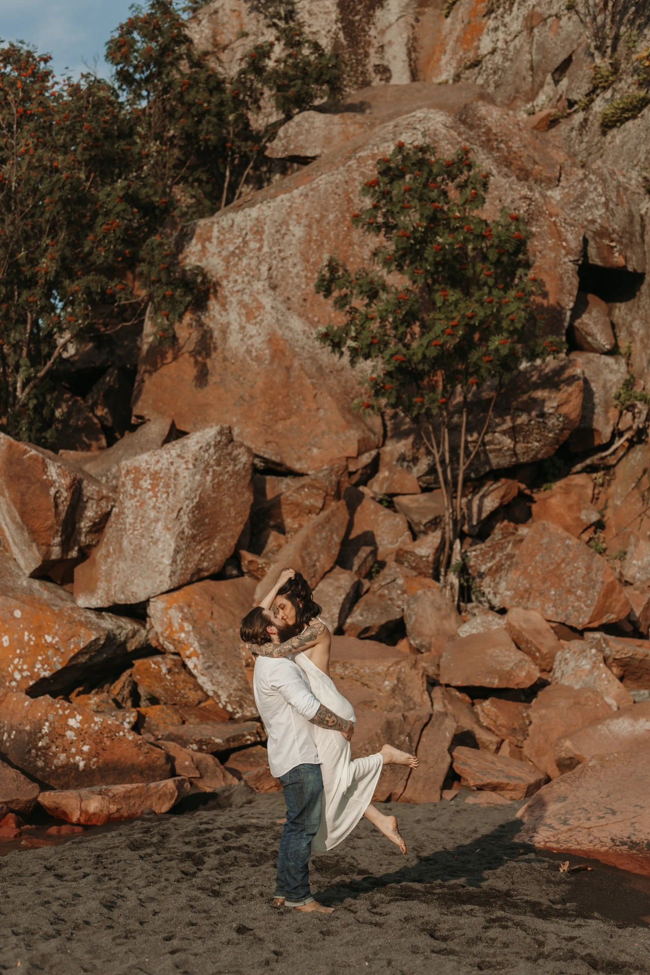 Groom lifting bride on rocky beach with boulders