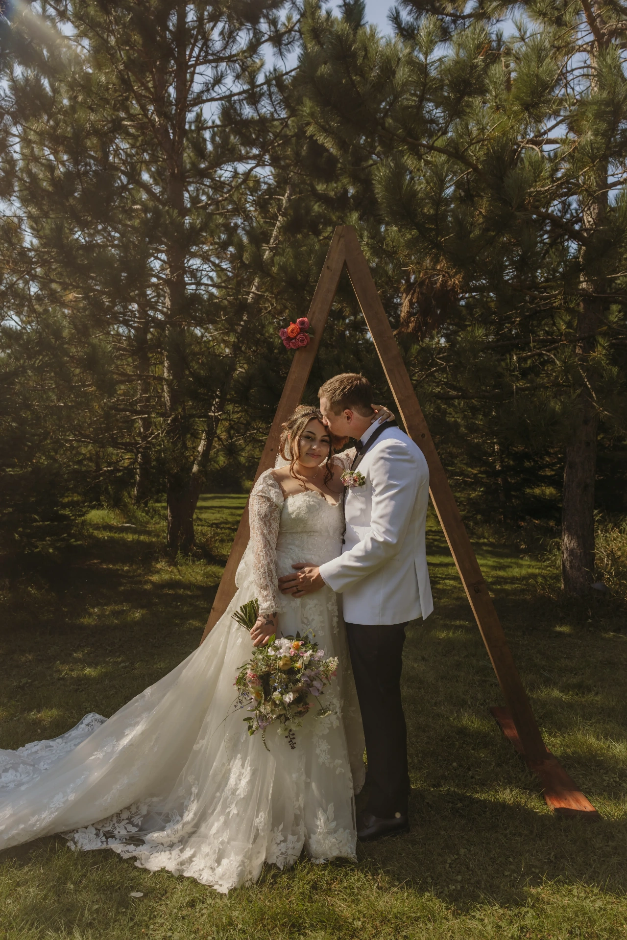Bride and groom under wooden triangle arch in pine trees