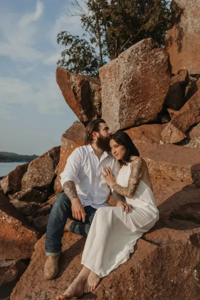 Couple sitting together on red rock boulders by lake — Mill City Museum, Minnesota wedding photography by Emma Ziegler, Honey Deww Photography