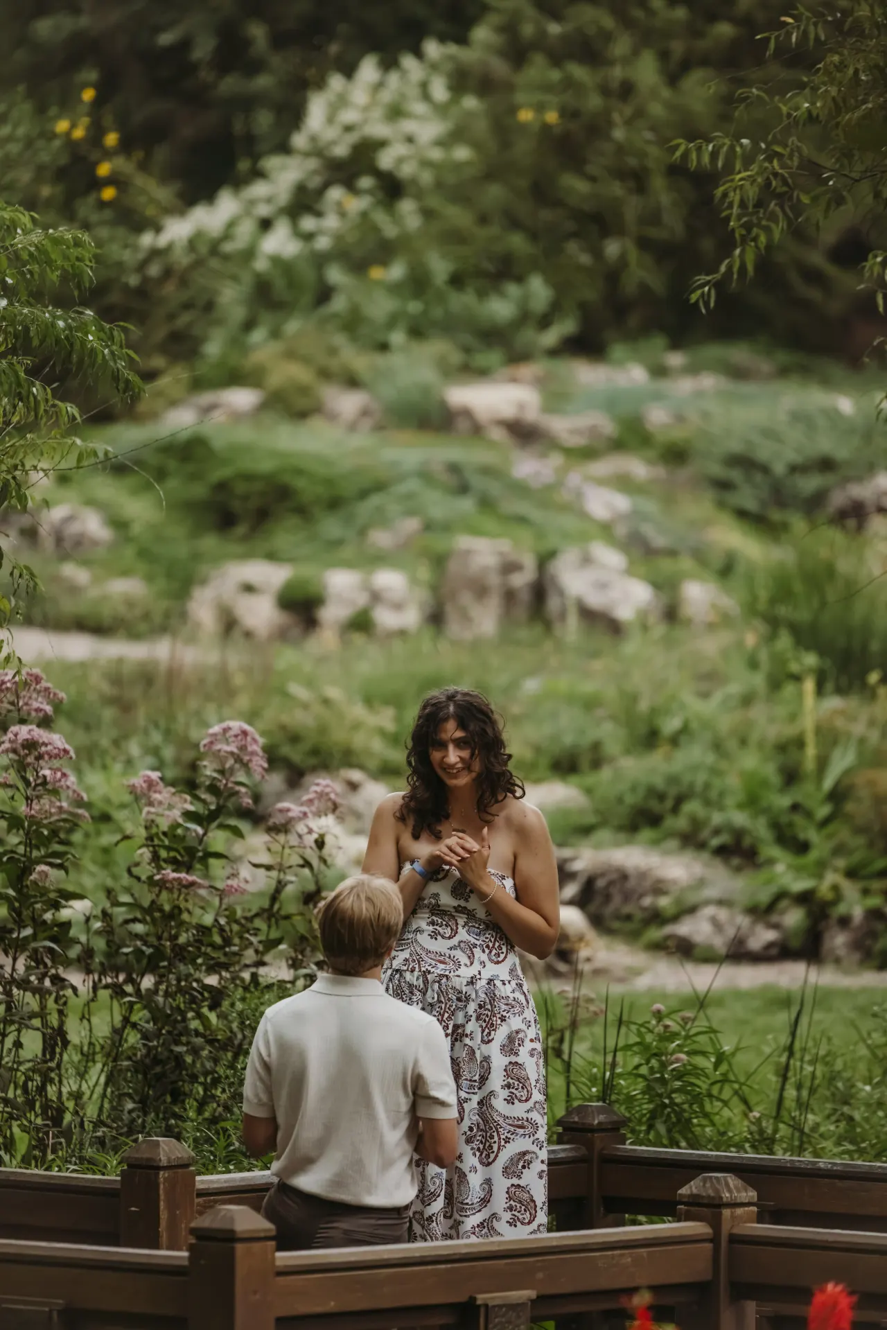 A proposal on a garden footbridge, one partner kneeling among tall summer flowers — Minneapolis & Twin Cities wedding photography by Emma Ziegler, Honey Deww Photography (Minnesota)
