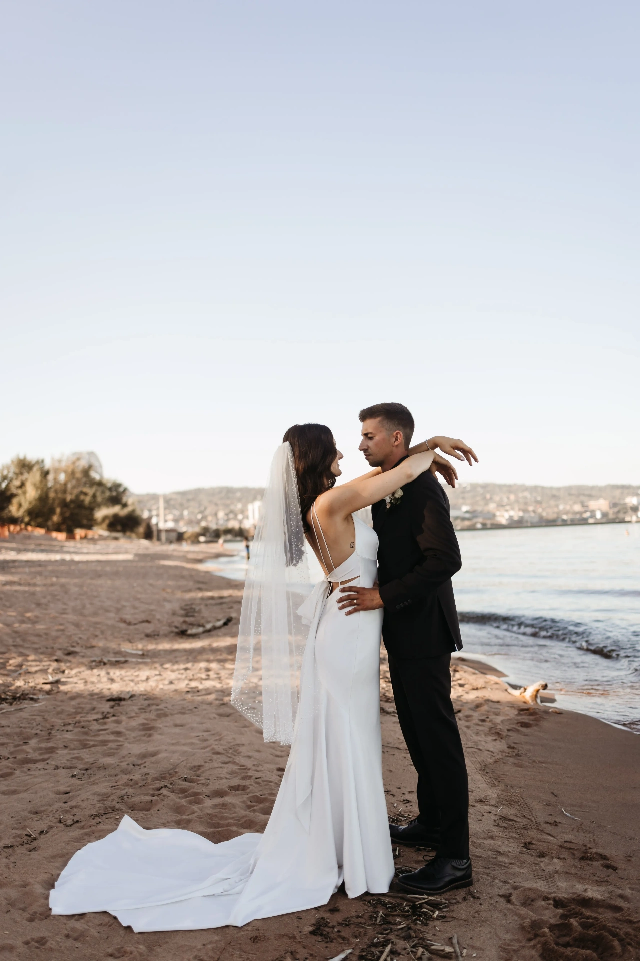 Bride and groom embracing on sandy beach at sunset
