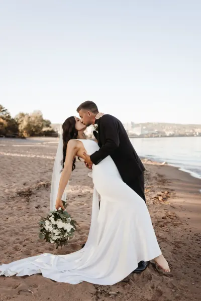 Groom dipping bride for a kiss on sandy beach with bouquet — Edina, Minnesota wedding photography by Emma Ziegler, Honey Deww Photography