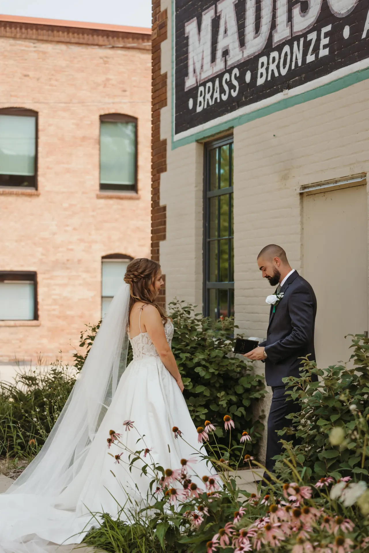 First look beside a painted brick warehouse wall, the bride's veil trailing behind her — Minneapolis & Twin Cities wedding photography by Emma Ziegler, Honey Deww Photography (Minnesota)