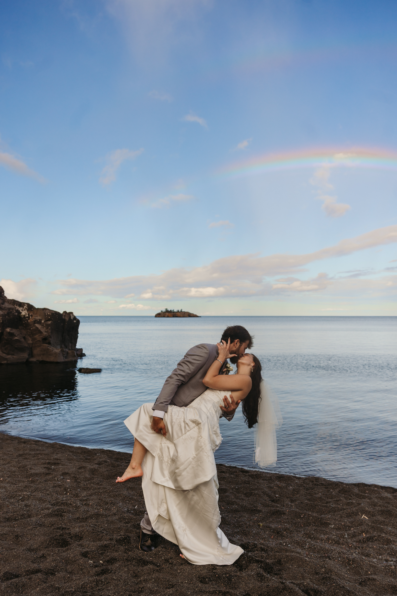 Couple kissing on beach with rainbow in sky