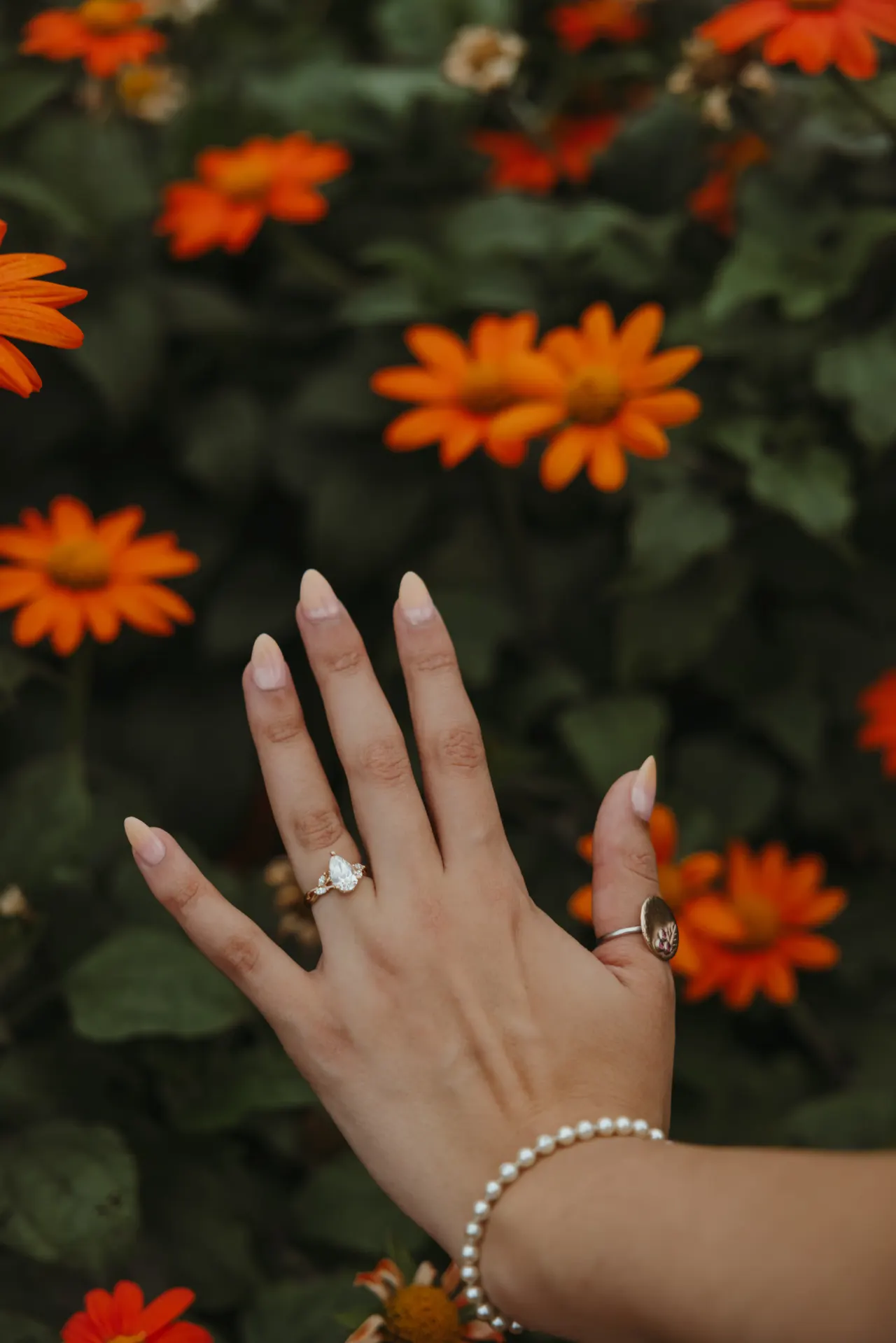 Engagement ring on a hand raised against a bed of orange zinnias — Minneapolis & Twin Cities wedding photography by Emma Ziegler, Honey Deww Photography (Minnesota)