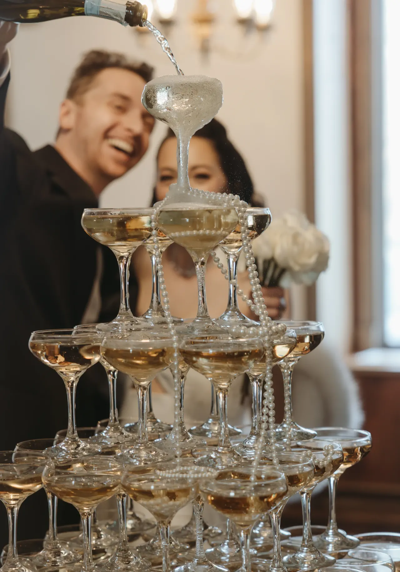 Champagne poured into a coupe tower as the couple watch and laugh behind it — Minneapolis & Twin Cities wedding photography by Emma Ziegler, Honey Deww Photography (Minnesota)