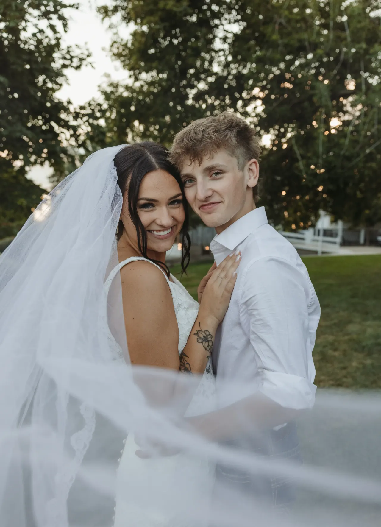 Bride and groom smiling as her veil lifts across the frame on an open lawn — Minneapolis & Twin Cities wedding photography by Emma Ziegler, Honey Deww Photography (Minnesota)