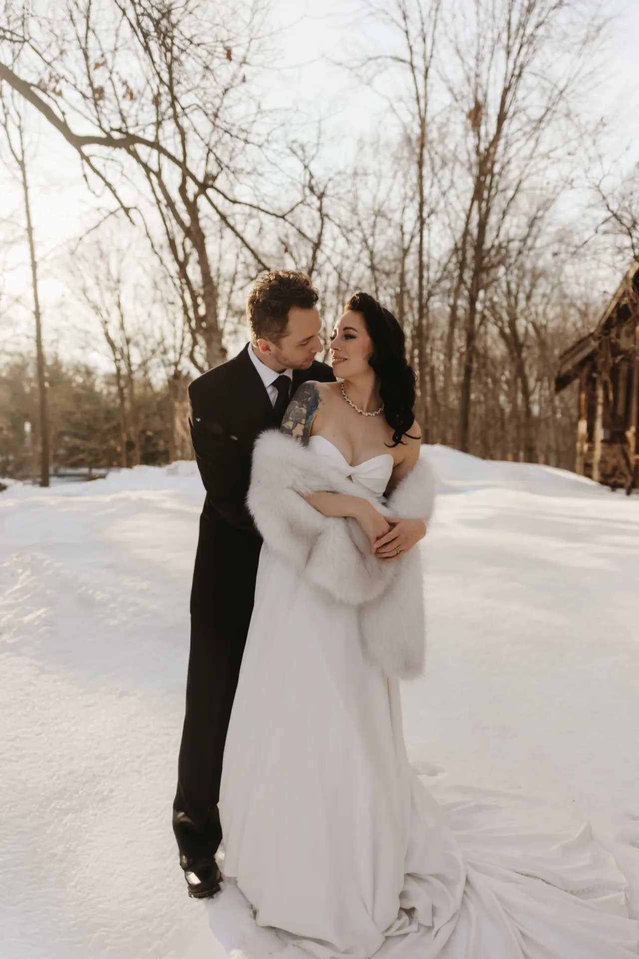 Bride wrapped in a white fur stole leaning into her groom on a snow-covered drive — Minneapolis & Twin Cities wedding photography by Emma Ziegler, Honey Deww Photography (Minnesota)