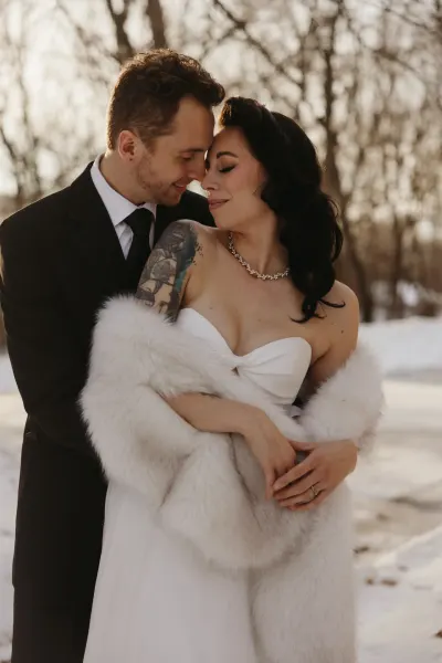 Bride in fur stole and groom in black suit embracing in snowy woods — Excelsior, Minnesota wedding photography by Emma Ziegler, Honey Deww Photography