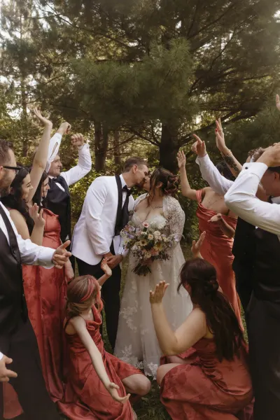 Wedding party cheering around kissing couple in pine grove — Downing, Minnesota wedding photography by Emma Ziegler, Honey Deww Photography