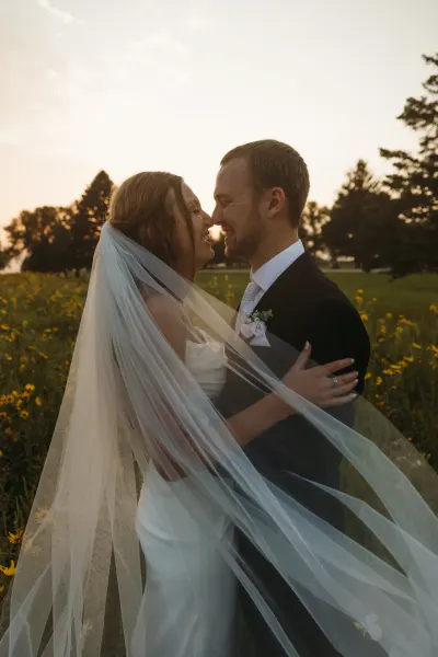 Couple embracing under flowing veil in sunlit wildflower field — Downing, Minnesota wedding photography by Emma Ziegler, Honey Deww Photography