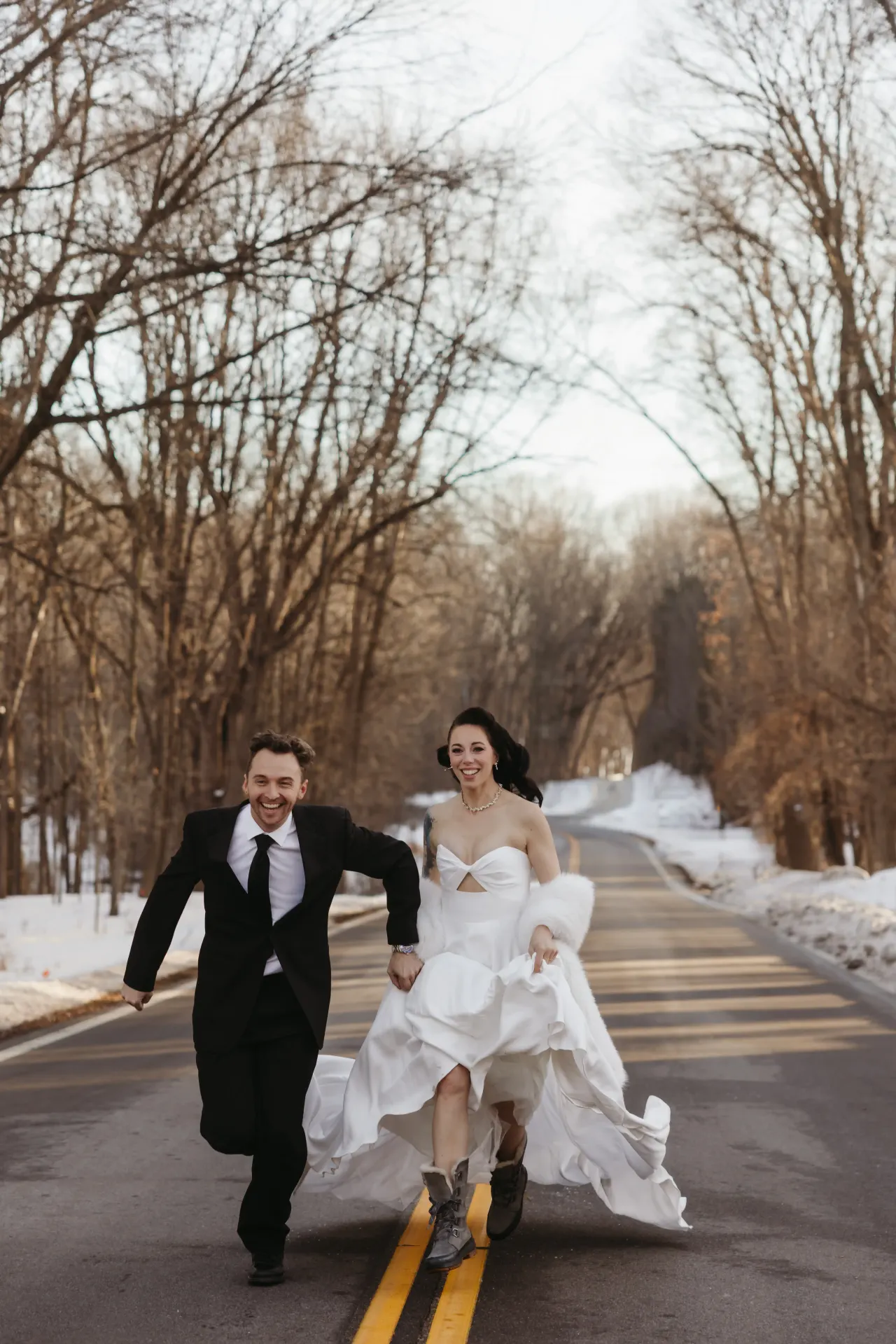 Bride and groom running hand in hand down a bare winter road, both laughing — Minneapolis & Twin Cities wedding photography by Emma Ziegler, Honey Deww Photography (Minnesota)