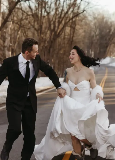 Bride laughing while running with groom on snowy tree-lined road — Aster Cafe, Minnesota wedding photography by Emma Ziegler, Honey Deww Photography