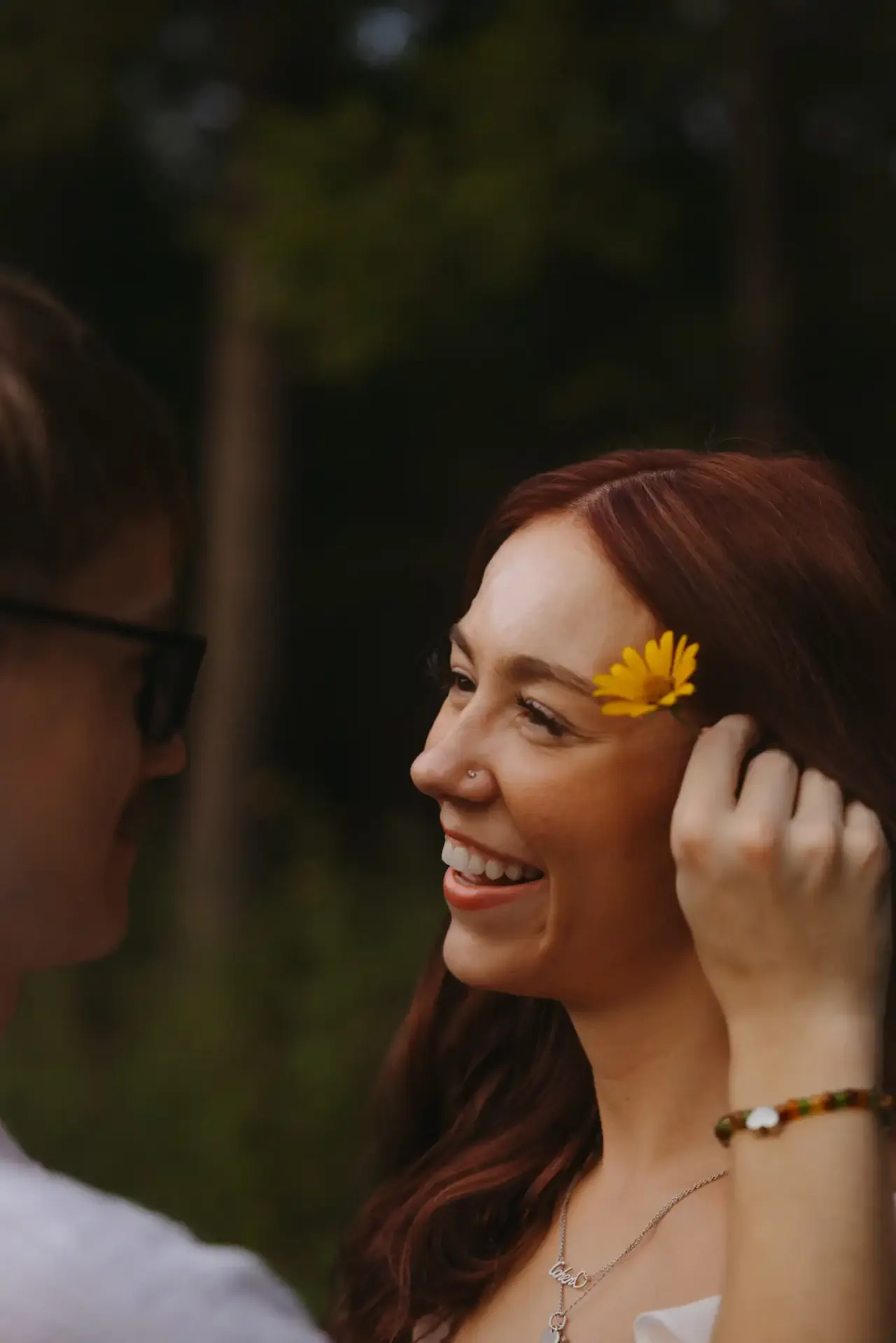One partner tucking a yellow wildflower behind the other's ear as she laughs — Minneapolis & Twin Cities wedding photography by Emma Ziegler, Honey Deww Photography (Minnesota)