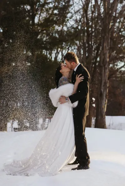 Bride in fur stole kissing groom as snow falls around them — Spring Park, Minnesota wedding photography by Emma Ziegler, Honey Deww Photography