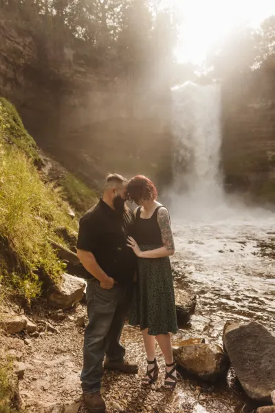 Couple embracing at base of misty waterfall in golden light — Spring Park, Minnesota wedding photography by Emma Ziegler, Honey Deww Photography