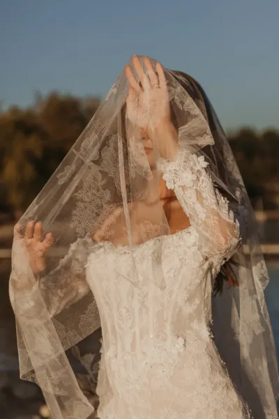 Bride lifting lace veil over face in golden sunlight by lake — Spring Park, Minnesota wedding photography by Emma Ziegler, Honey Deww Photography