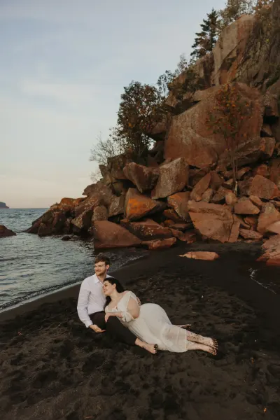 Couple resting on black sand beach with rocky cliff backdrop — St. Francis, Minnesota wedding photography by Emma Ziegler, Honey Deww Photography
