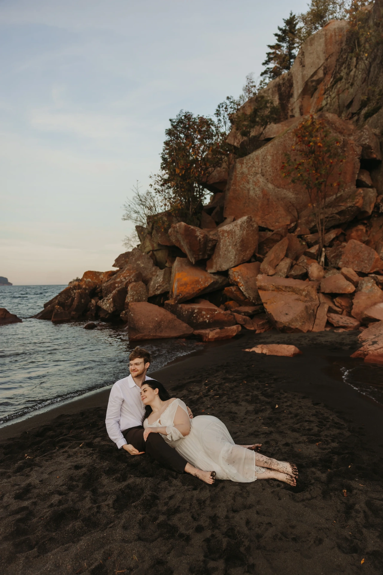 Couple resting on black sand beach with rocky cliff backdrop — Minneapolis & Twin Cities wedding photography by Emma Ziegler, Honeydew Photography (Minnesota)