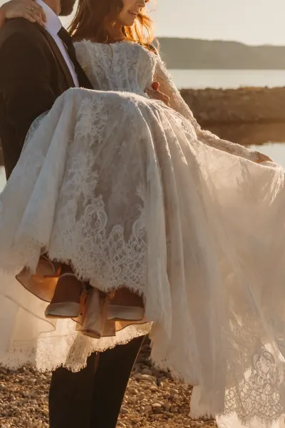Close-up of lace wedding dress being carried on rocky lakeshore at golden hour — St. Francis, Minnesota wedding photography by Emma Ziegler, Honey Deww Photography