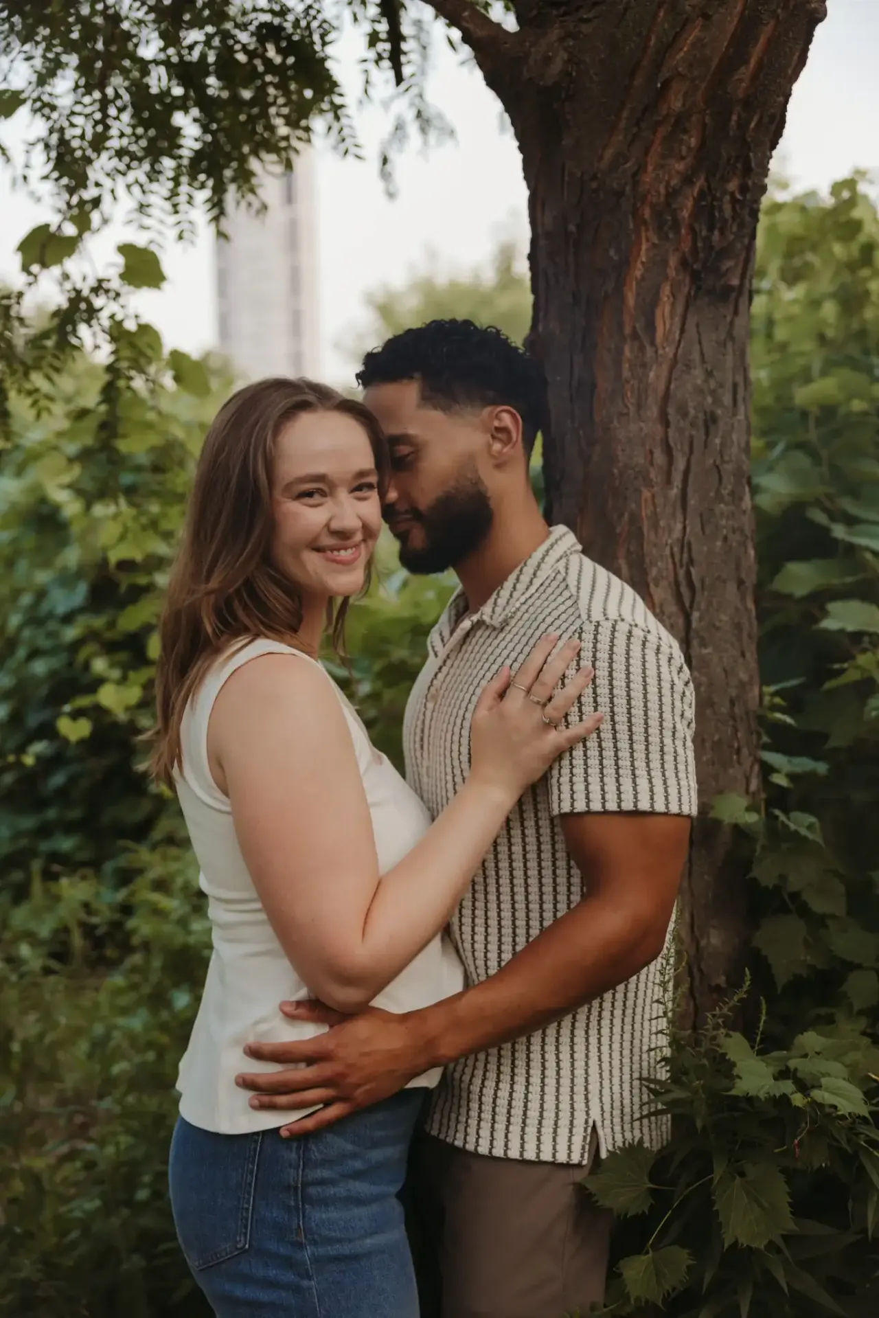 Couple embracing against a broad tree trunk in a summer park — Minneapolis & Twin Cities wedding photography by Emma Ziegler, Honey Deww Photography (Minnesota)
