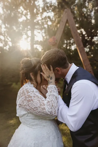 Bride and groom kissing under wooden A-frame arch with sunburst — Baldwin, Minnesota wedding photography by Emma Ziegler, Honey Deww Photography