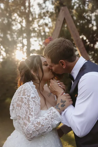 Bride and groom kissing under wooden arch with butterfly tattoo detail — Baldwin, Minnesota wedding photography by Emma Ziegler, Honey Deww Photography