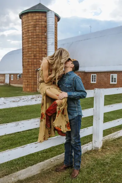 Country couple kissing by white fence with barn and silo — the Heritage Center of Brooklyn Center, Minnesota wedding photography by Emma Ziegler, Honey Deww Photography