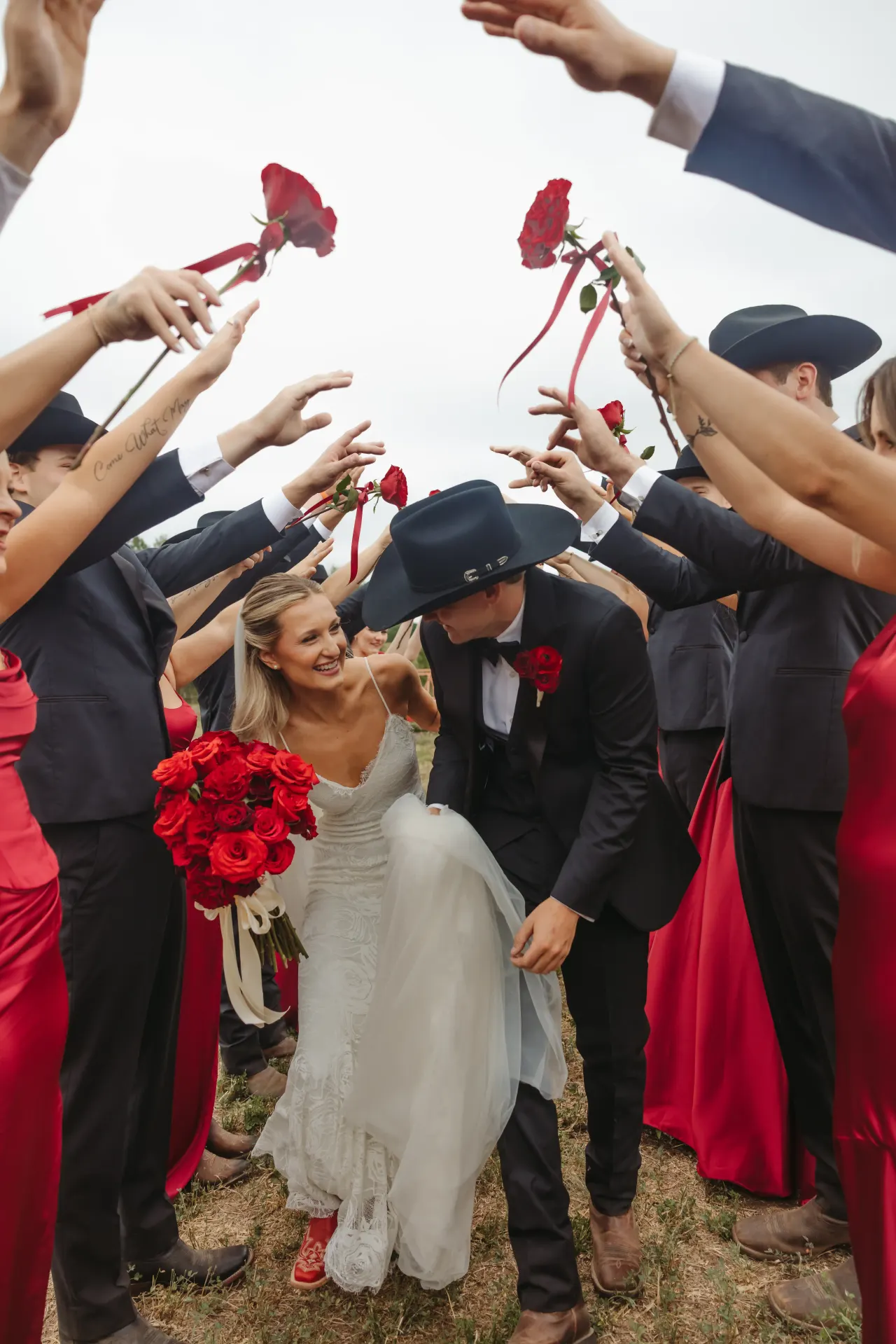 Wedding party raising long-stemmed red roses over a dipping bride and groom in cowboy hats — Minneapolis & Twin Cities wedding photography by Emma Ziegler, Honey Deww Photography (Minnesota)