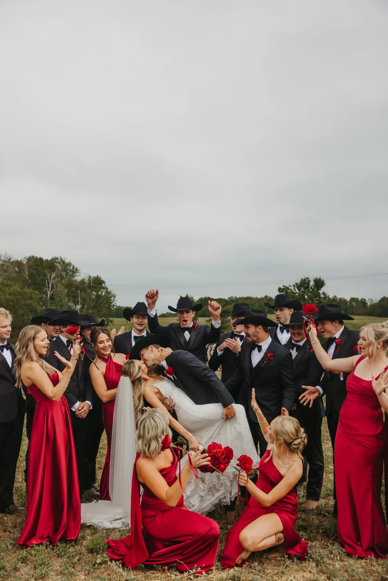 Wedding party in red gowns and black hats cheering as the couple dip into a kiss — Minneapolis & Twin Cities wedding photography by Emma Ziegler, Honey Deww Photography (Minnesota)