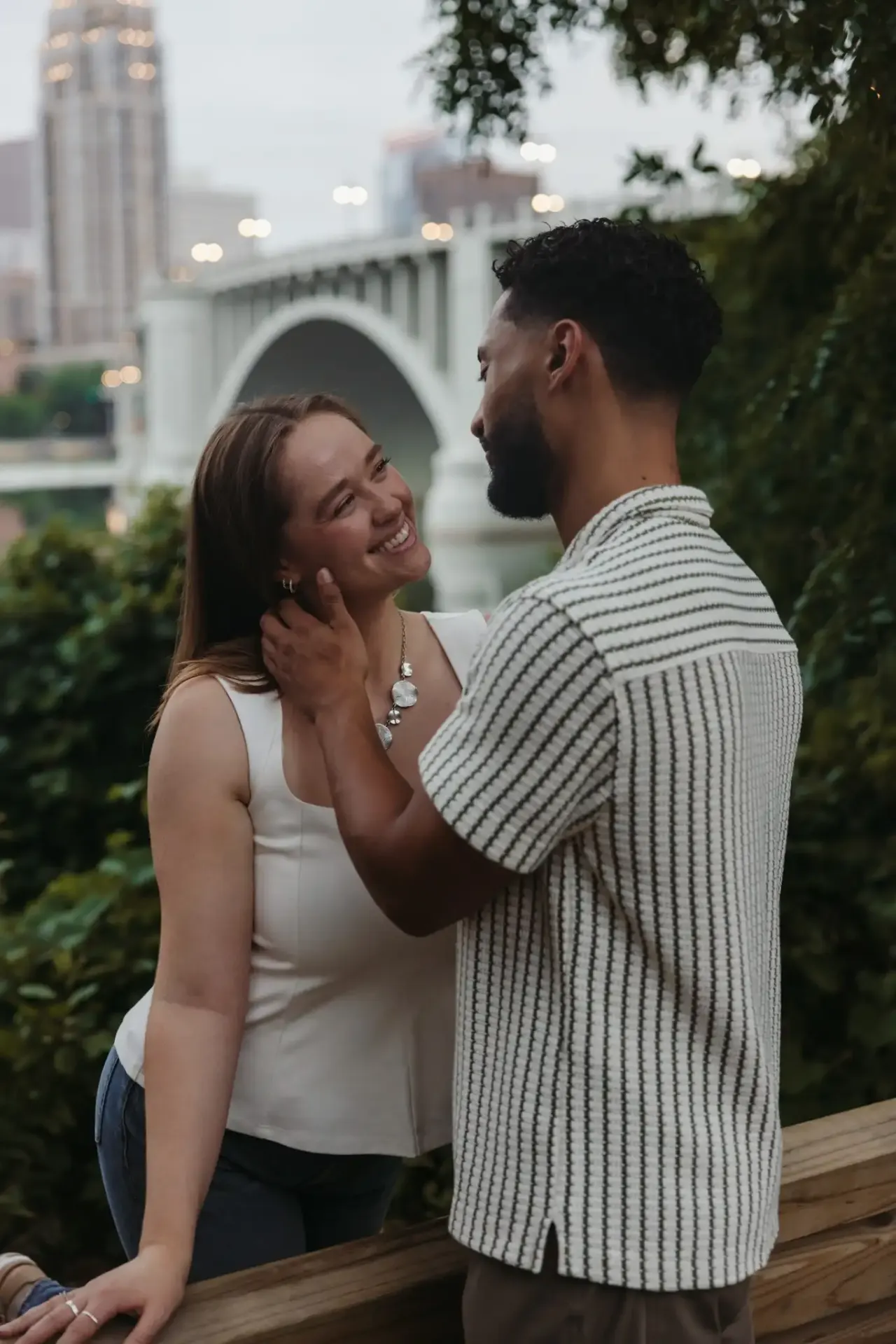 One partner resting a hand on the other's cheek with a river bridge behind them — Minneapolis & Twin Cities wedding photography by Emma Ziegler, Honey Deww Photography (Minnesota)