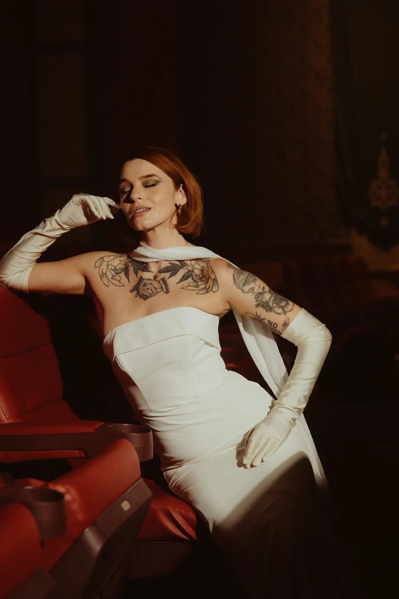 Bride in a satin gown and opera gloves reclining across red theatre seats — Minneapolis & Twin Cities wedding photography by Emma Ziegler, Honey Deww Photography (Minnesota)