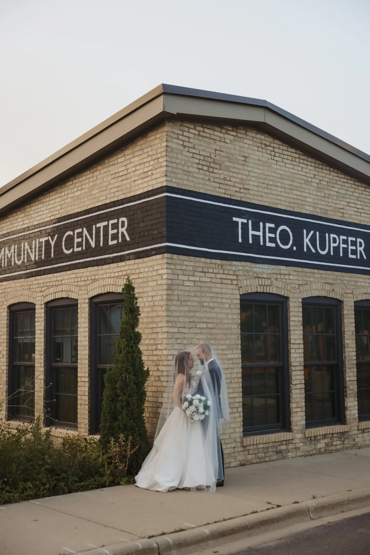 Bride and groom kissing at the corner of a cream brick community building — Minneapolis & Twin Cities wedding photography by Emma Ziegler, Honey Deww Photography (Minnesota)