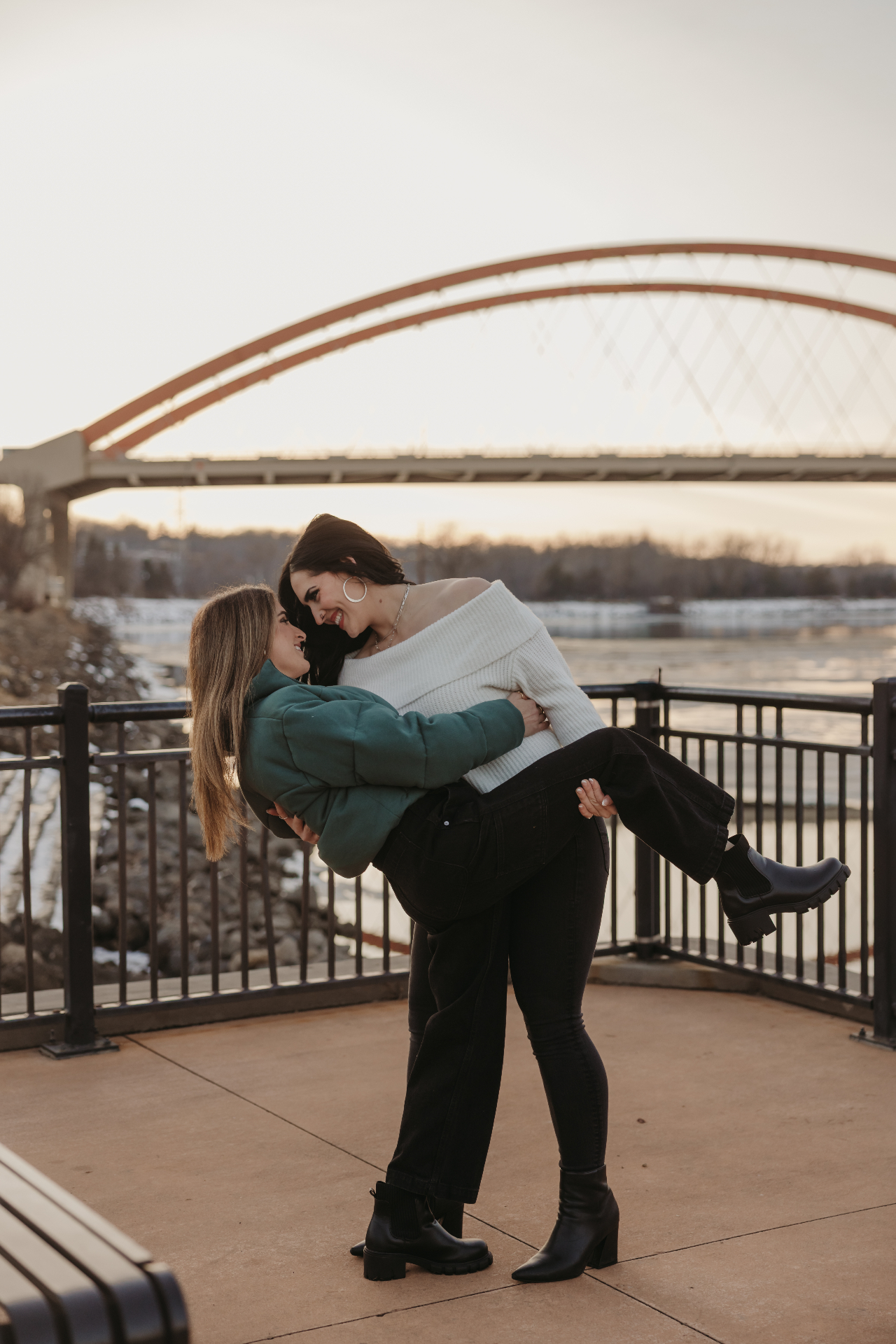 Couple playfully lifting each other by a bridge at golden hour