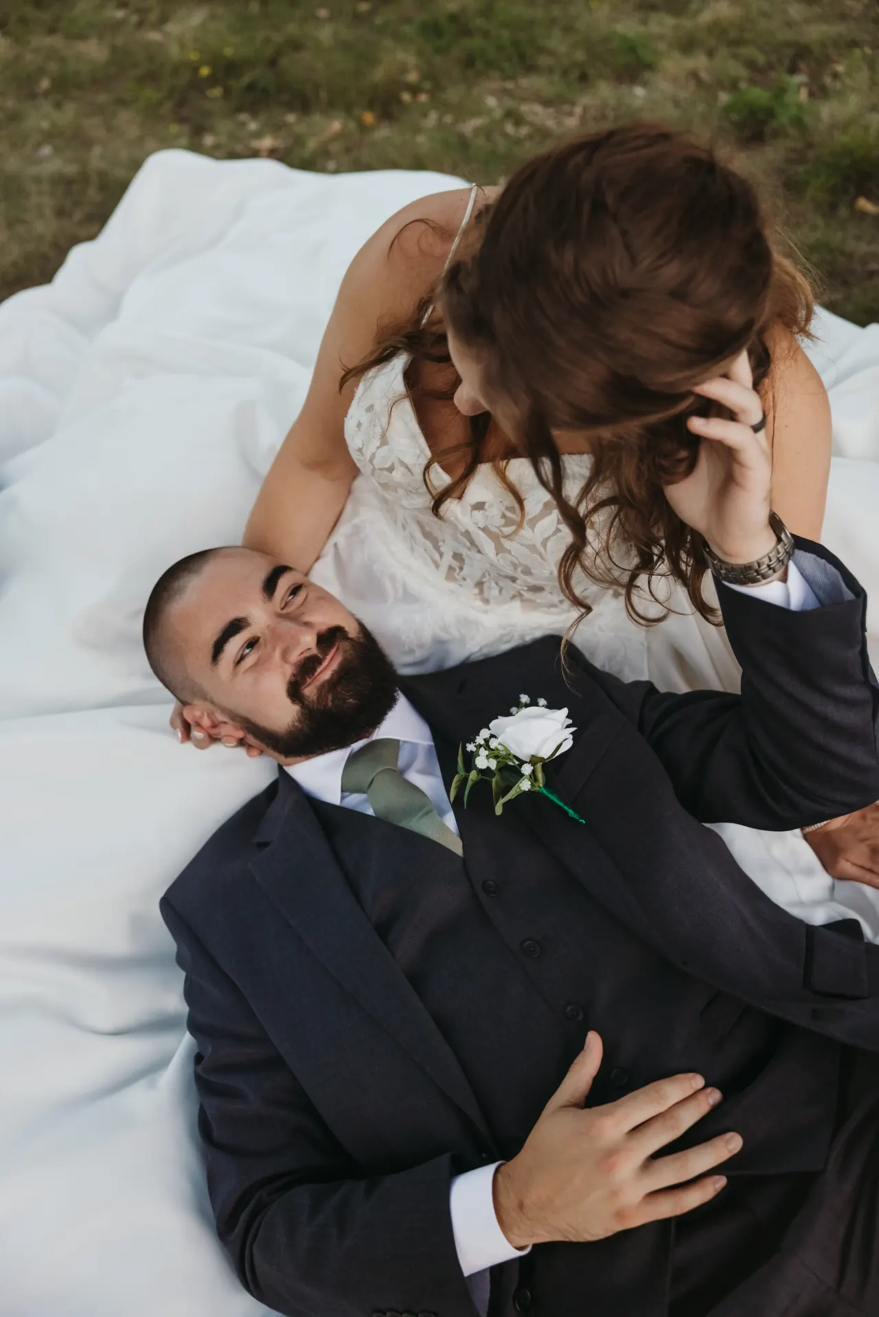 Bride leaning over her groom as he lies back on a white blanket on the grass — Minneapolis & Twin Cities wedding photography by Emma Ziegler, Honey Deww Photography (Minnesota)