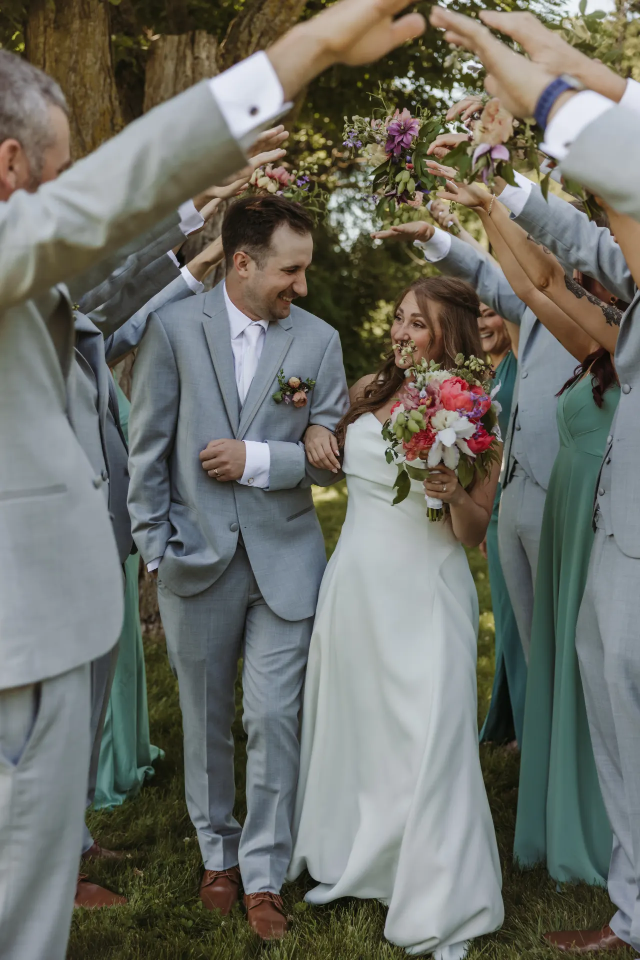 Bride and groom walking through an arch of raised bouquets, laughing — Minneapolis & Twin Cities wedding photography by Emma Ziegler, Honey Deww Photography (Minnesota)