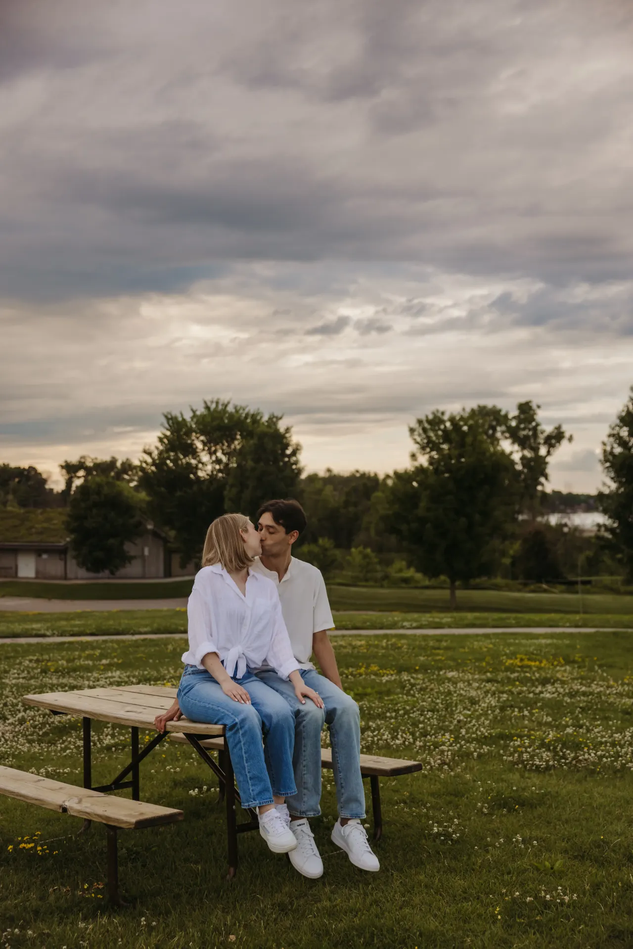 Couple sitting on a picnic table under a wide, cloud-heavy sky — Minneapolis & Twin Cities wedding photography by Emma Ziegler, Honey Deww Photography (Minnesota)
