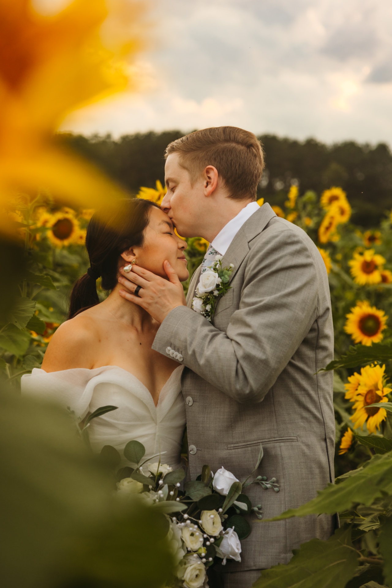 Groom kissing bride on forehead in sunflower field