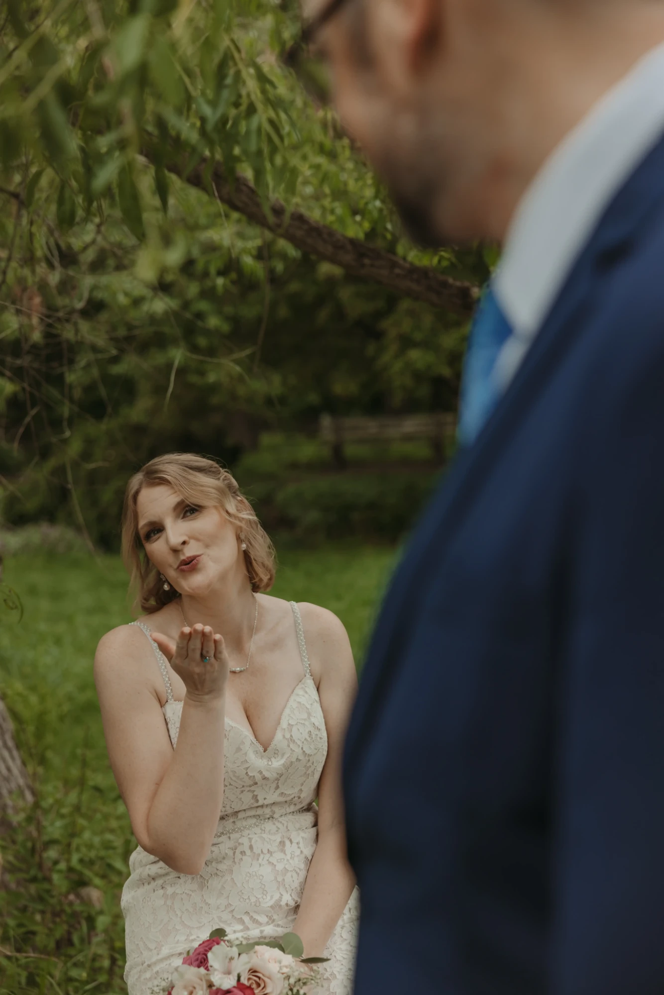 Bride blowing a kiss toward the groom, who is out of focus in the foreground