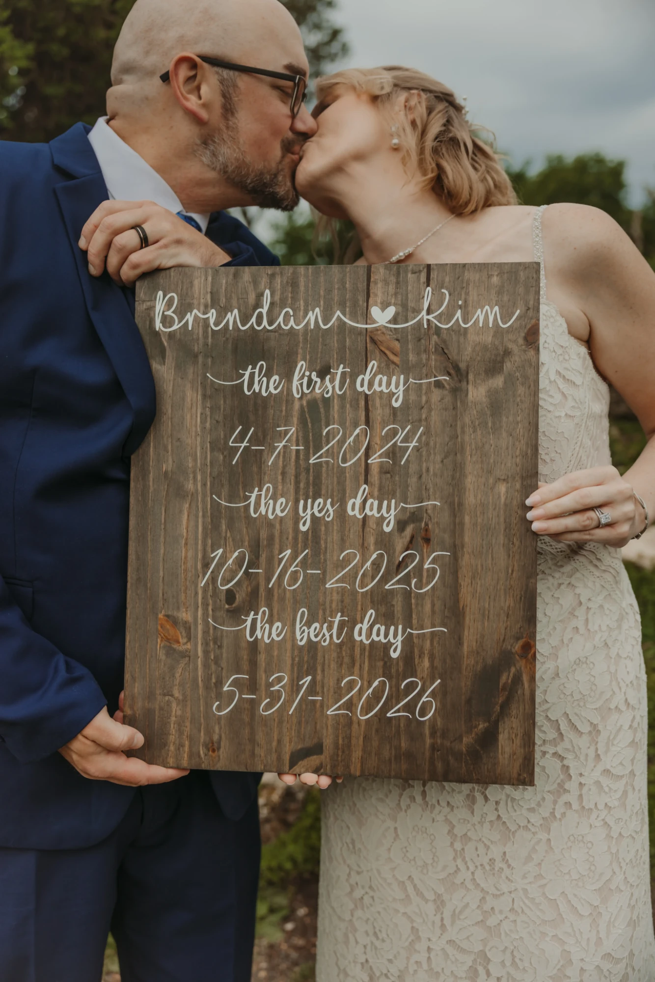 Couple kissing behind their wooden sign with the three dates at Lyndale Park Rose Garden